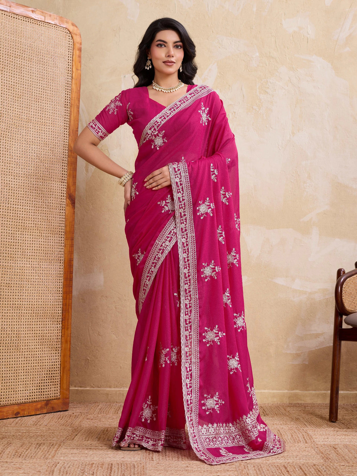 Woman wearing a pink saree with white patterns against a beige wall.