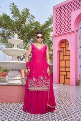 Woman in a pink traditional outfit standing in front of a pink architectural structure and fountain.
