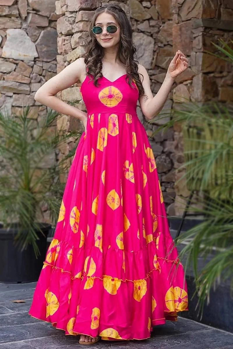 Woman wearing a bright pink dress with yellow patterns against a stone wall.
