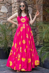 Woman wearing a bright pink dress with yellow patterns against a stone wall.