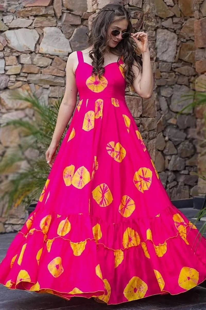 Woman wearing a bright pink dress with yellow floral patterns against a stone wall.
