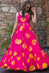 Woman wearing a bright pink dress with yellow floral patterns against a stone wall.