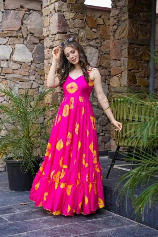 Woman in a pink dress with yellow patterns standing outdoors against a stone wall.