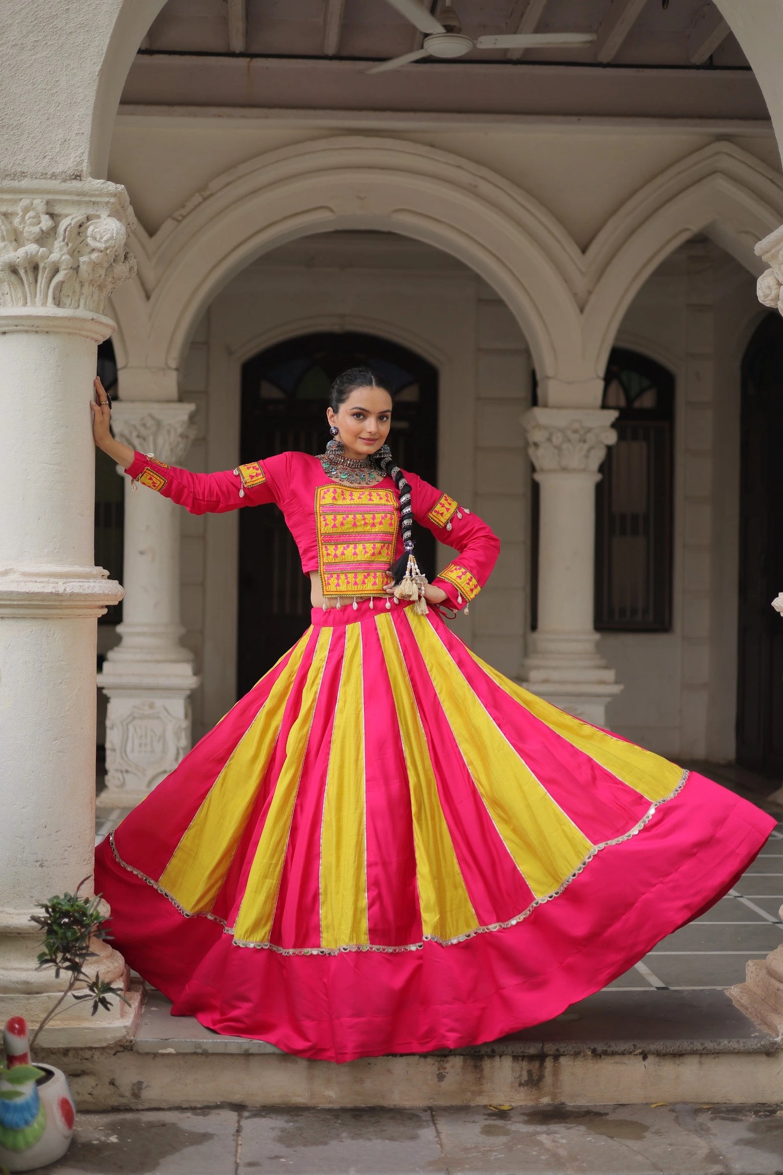 Woman in a vibrant pink and yellow traditional outfit standing in an architectural setting.