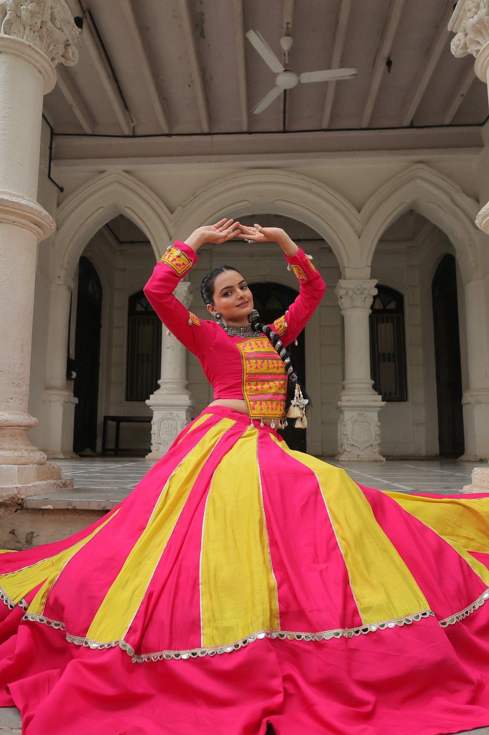 Woman in a vibrant pink and yellow traditional outfit performing in an architectural setting.