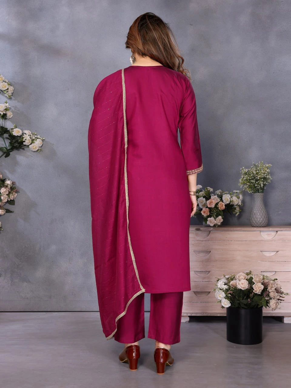 Woman in a magenta traditional outfit standing against a gray wall with decorative elements.