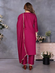 Woman in a magenta traditional outfit standing against a gray wall with decorative elements.