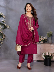 Woman in a magenta traditional outfit with embroidery, standing against a gray background with decorative elements.