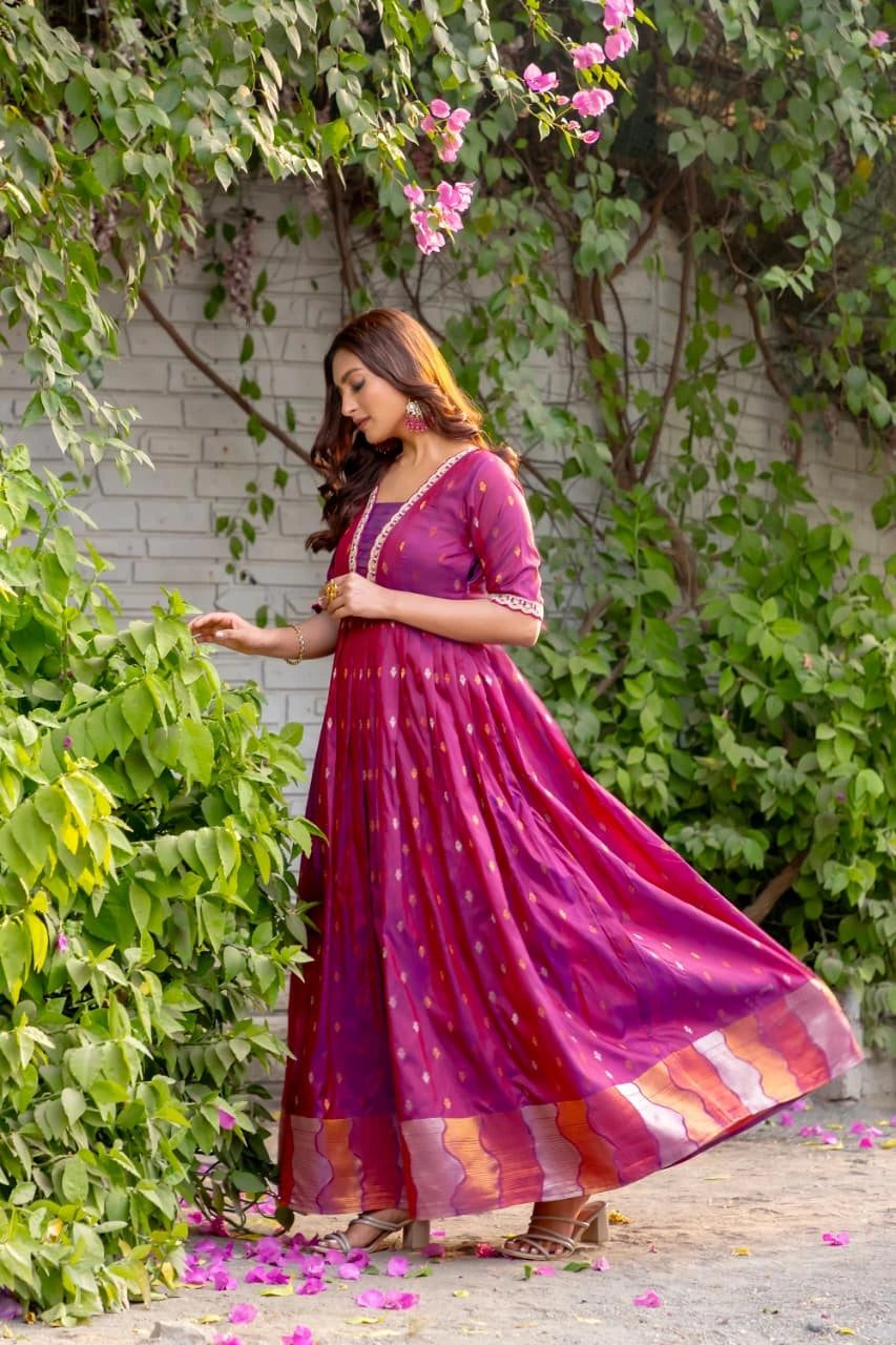 Woman in a vibrant purple dress standing outdoors with greenery and flowers.