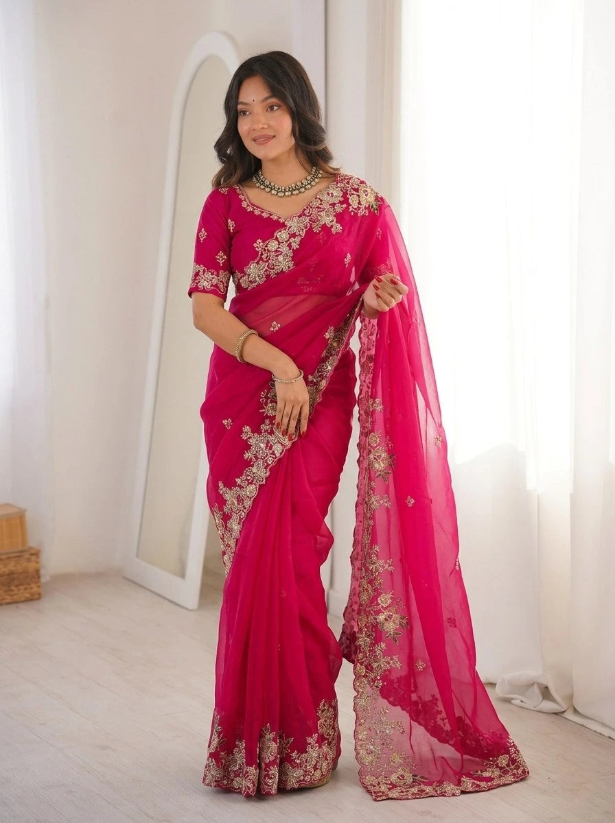 Woman wearing a bright pink saree with gold embroidery in a room.