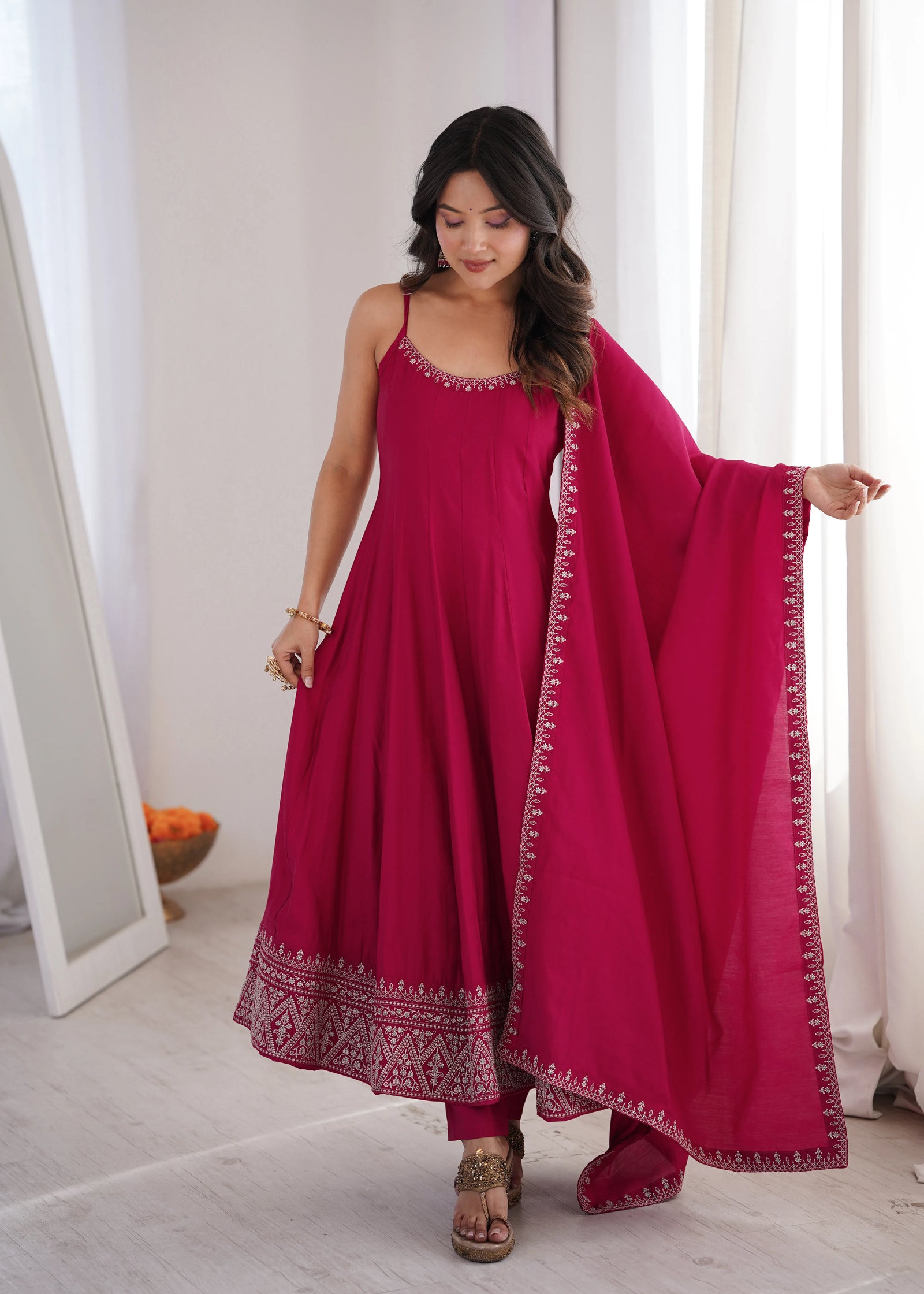 Woman wearing a pink traditional outfit with a matching dupatta in a bright room.