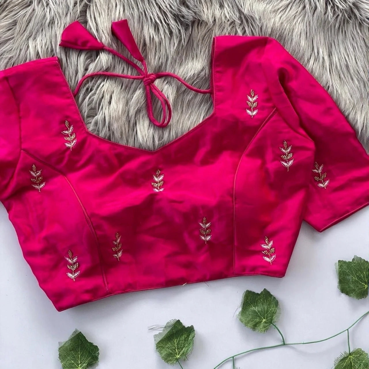 Pink blouse with floral embroidery on a textured surface with green leaves.
