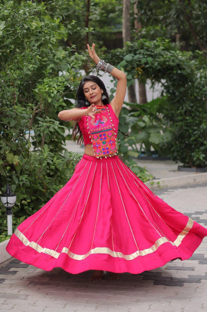 Woman in a bright pink traditional outfit with gold accents dancing outdoors.