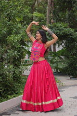 Woman in a bright pink traditional outfit with colorful top dancing outdoors.