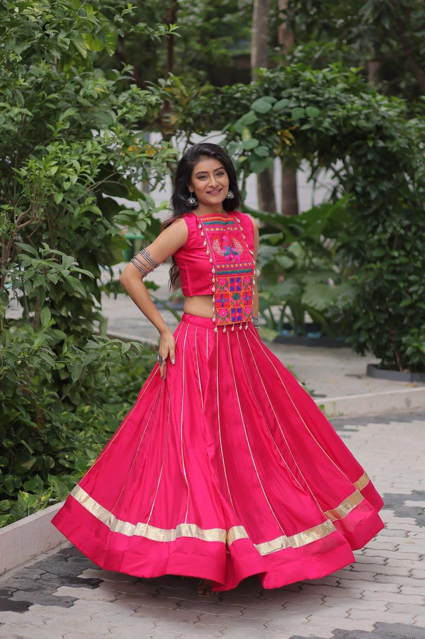 Woman in a bright pink traditional outfit with colorful embroidery standing outdoors.