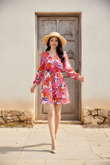 Woman in a floral dress and hat standing in front of a wooden door.