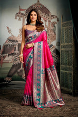 Woman in a pink saree with intricate patterns standing in front of an ornate wall.