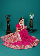 Woman in a pink saree standing against a teal background with decorative elements.
