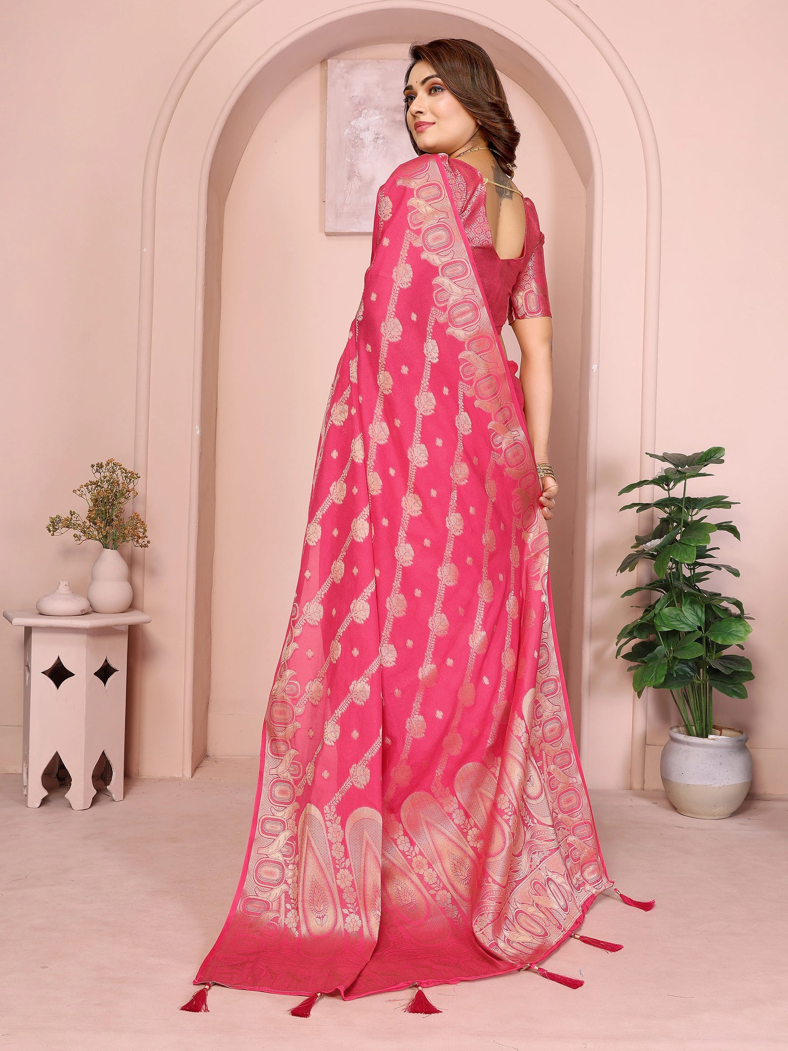 Woman wearing a pink saree with white patterns in a decorated room.