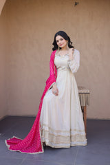 Woman in a white traditional outfit with a pink dupatta against a plain wall.