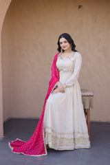 Woman in a white and pink traditional outfit standing against a beige wall.
