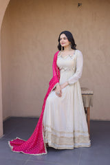 Woman in a white traditional outfit with a pink dupatta standing against a beige wall.