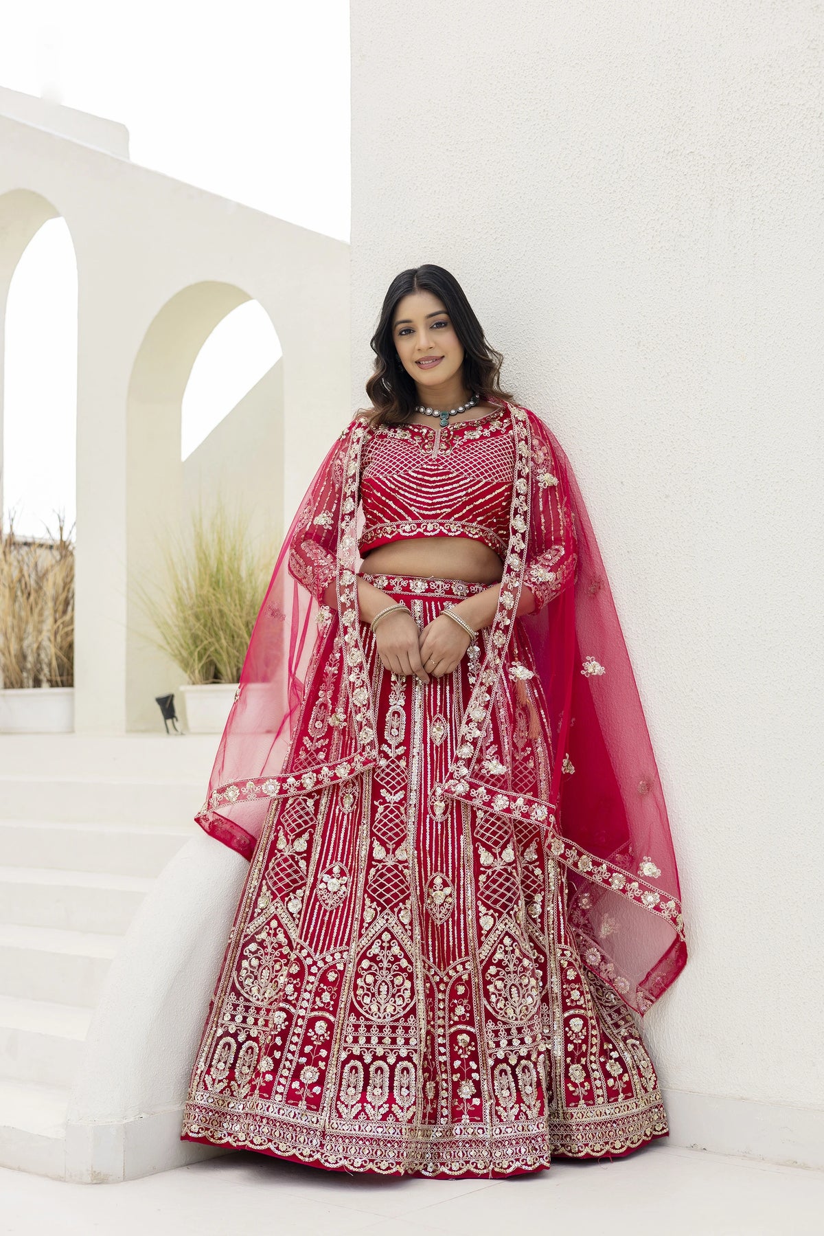 Woman in a red and gold embroidered traditional outfit standing against a white background.