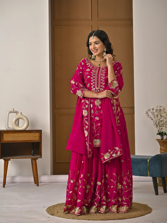 Woman in a pink traditional outfit with gold embroidery in a room setting.