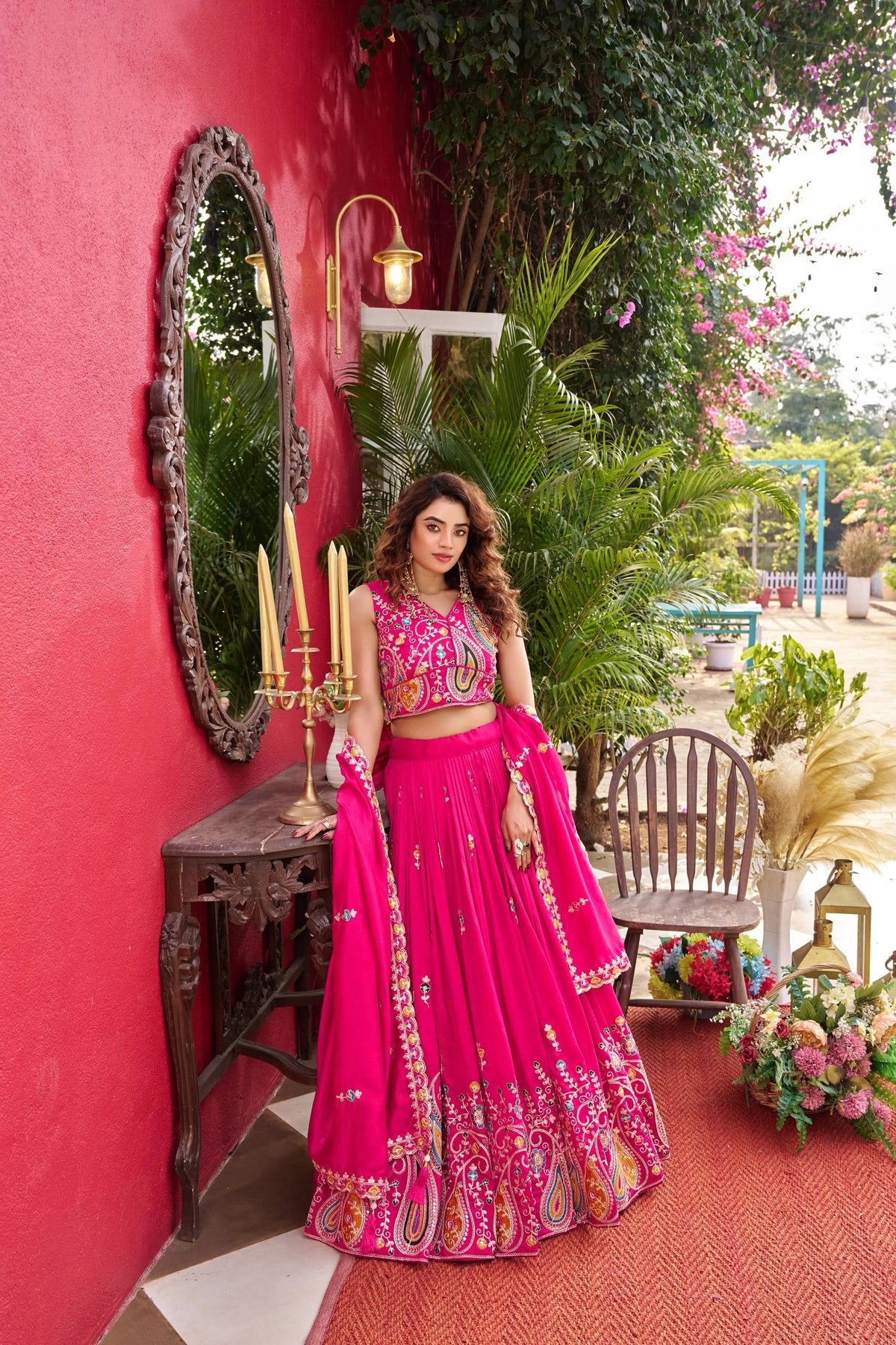 Woman in a pink traditional outfit standing in front of a red wall with decorative elements.