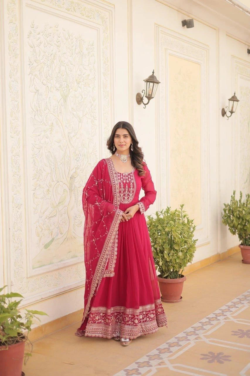 Woman in a red traditional outfit standing in a decorated room with plants.