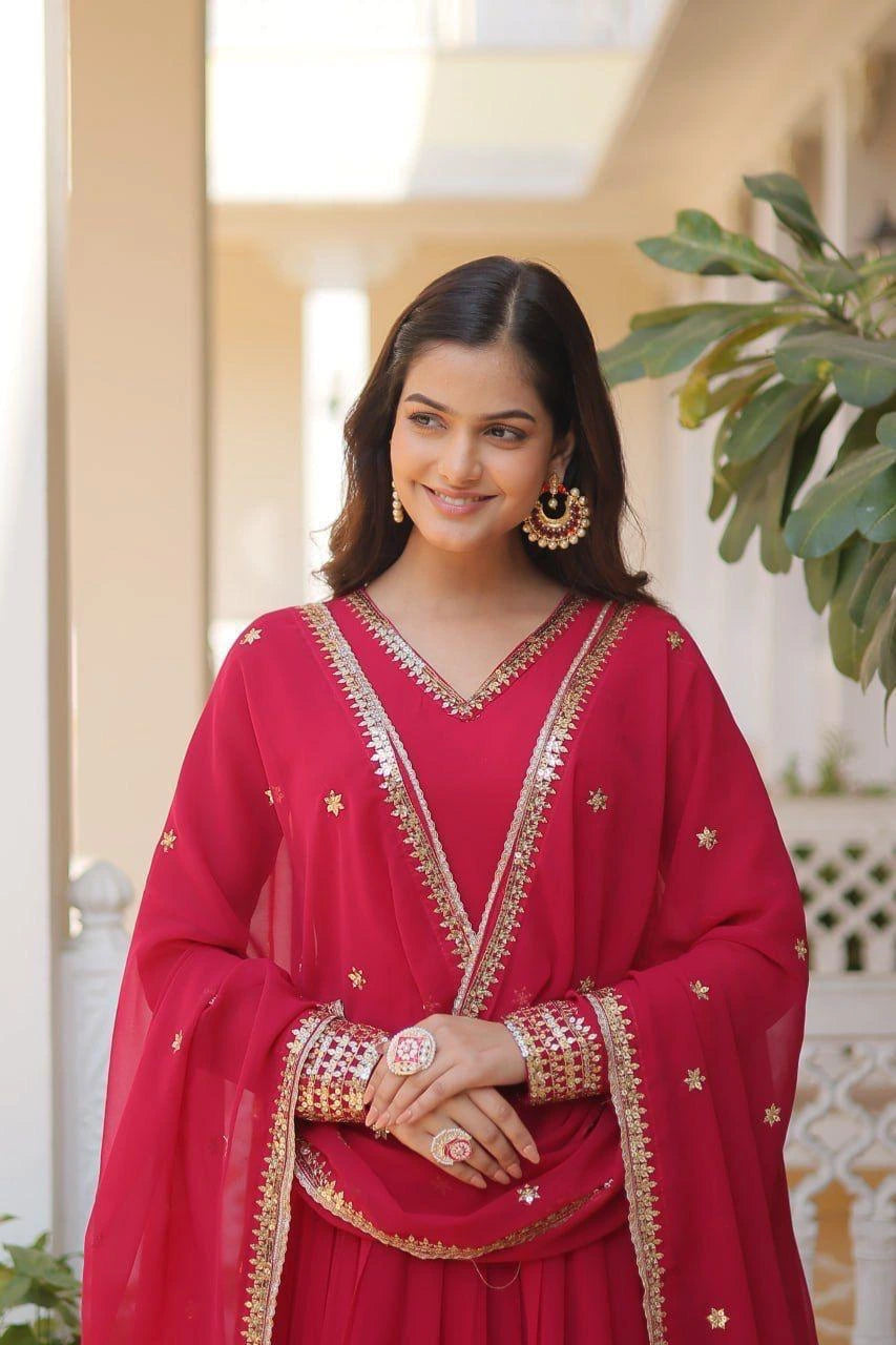 Woman in a red traditional outfit with gold details standing indoors.