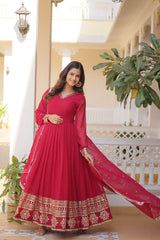 Woman in a red anarkali suit standing in a well-lit room with plants and architectural elements.