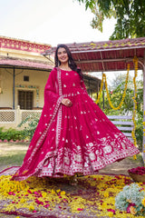 Woman in a pink traditional outfit standing outdoors with floral decorations.