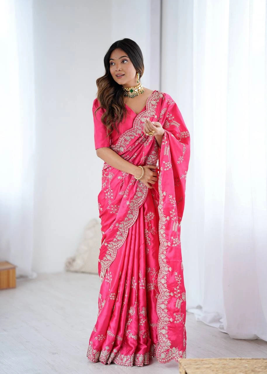 Woman wearing a bright pink saree with white patterns in a minimal indoor setting.