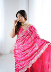 Woman wearing a bright pink saree with intricate designs on a plain background