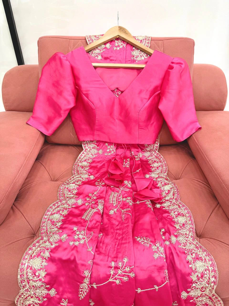 Pink embroidered dress on a hanger against a pink couch.