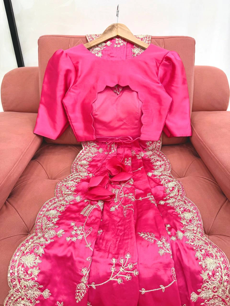 Pink embroidered dress on a hanger against a pink couch.