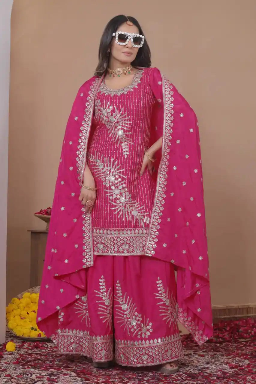 Woman wearing a pink traditional outfit with white embroidery against a beige wall.