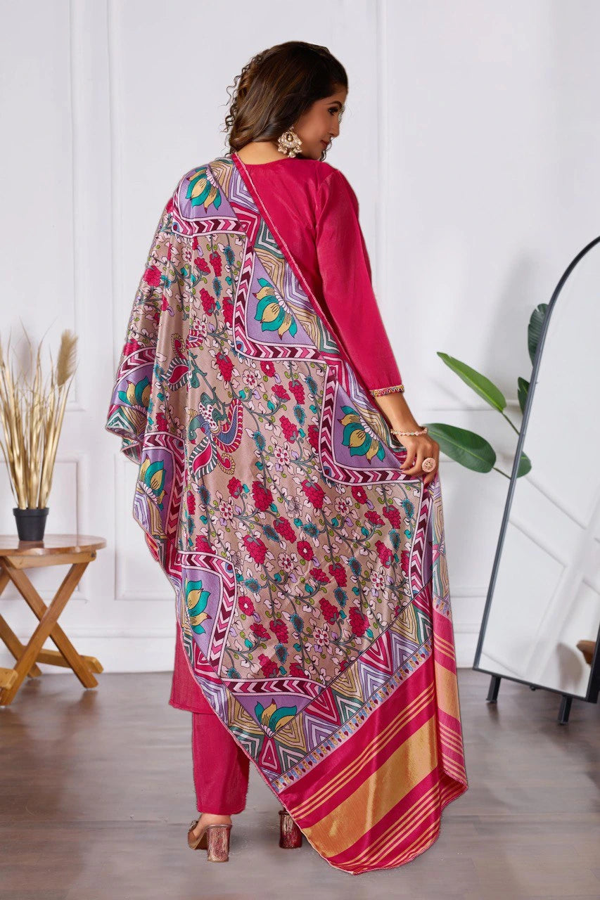 Woman wearing a colorful traditional outfit with a patterned dupatta in a minimal indoor setting.