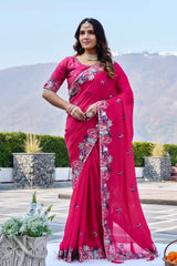 Woman wearing a pink saree with floral patterns in an outdoor setting.