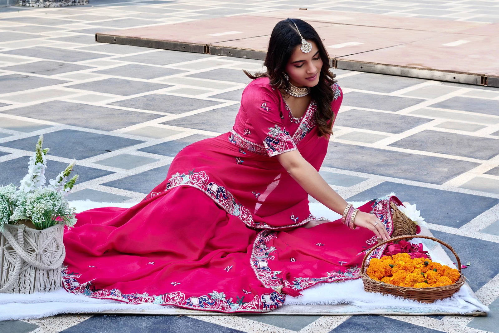 Woman in a pink traditional outfit arranging flowers on a stone pavement.
