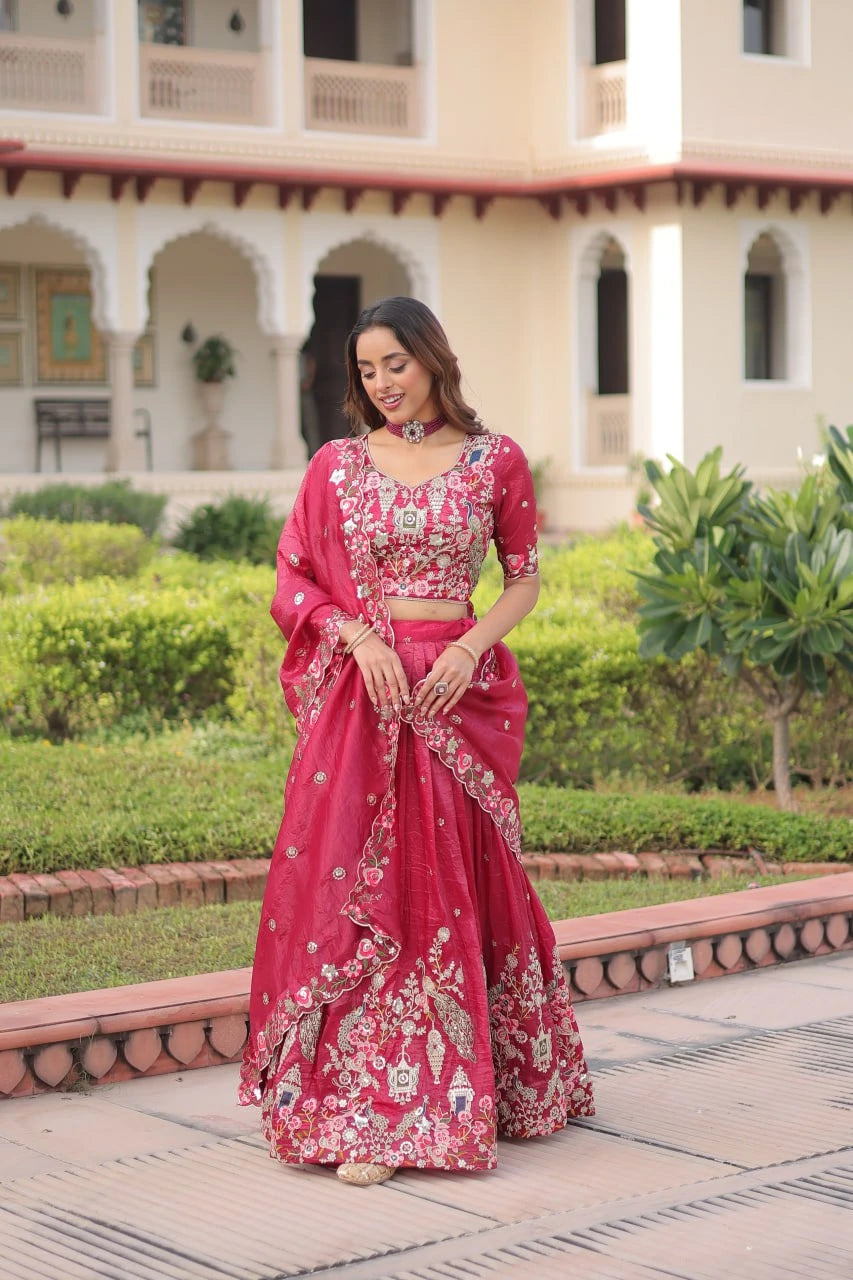 Woman in a pink traditional outfit standing in front of a building with greenery.