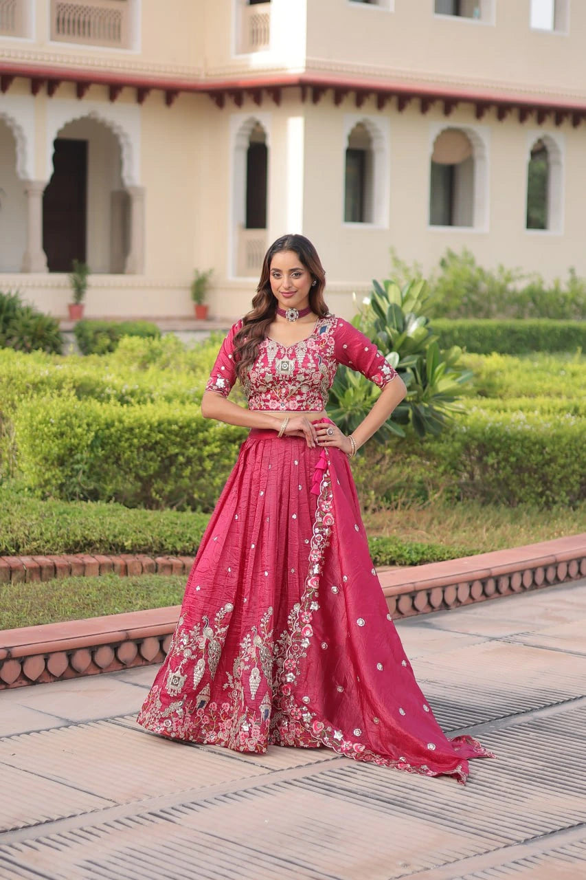 Woman in a pink traditional outfit standing in front of an architectural building with greenery.