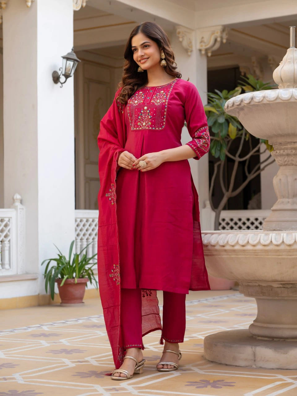 Woman in a pink traditional outfit standing in an outdoor setting with decorative elements.