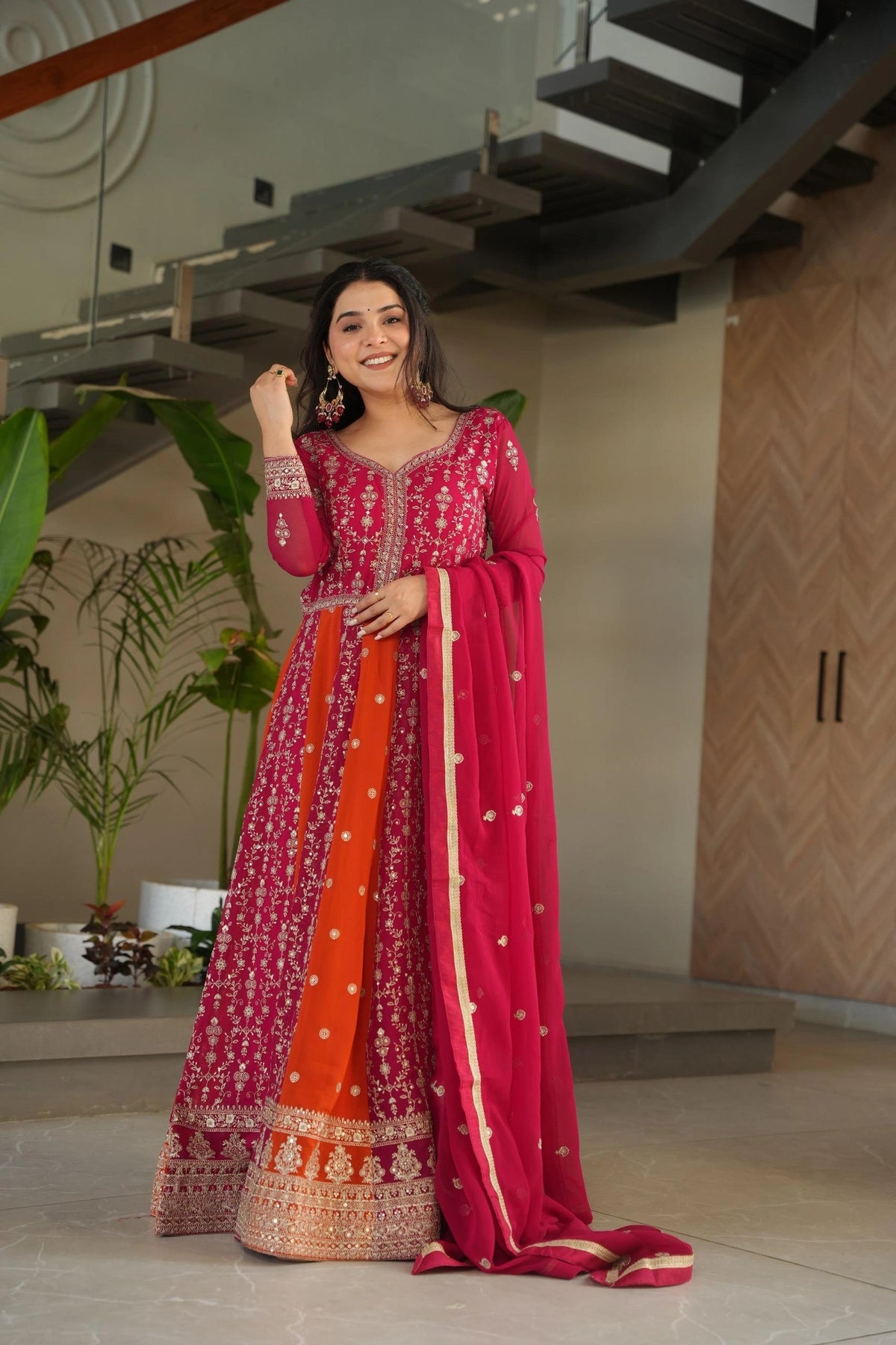Woman in a vibrant traditional outfit with a pink and orange design, standing indoors.