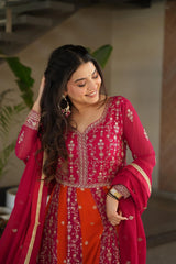 Woman in a red and orange traditional outfit with intricate patterns, standing indoors.