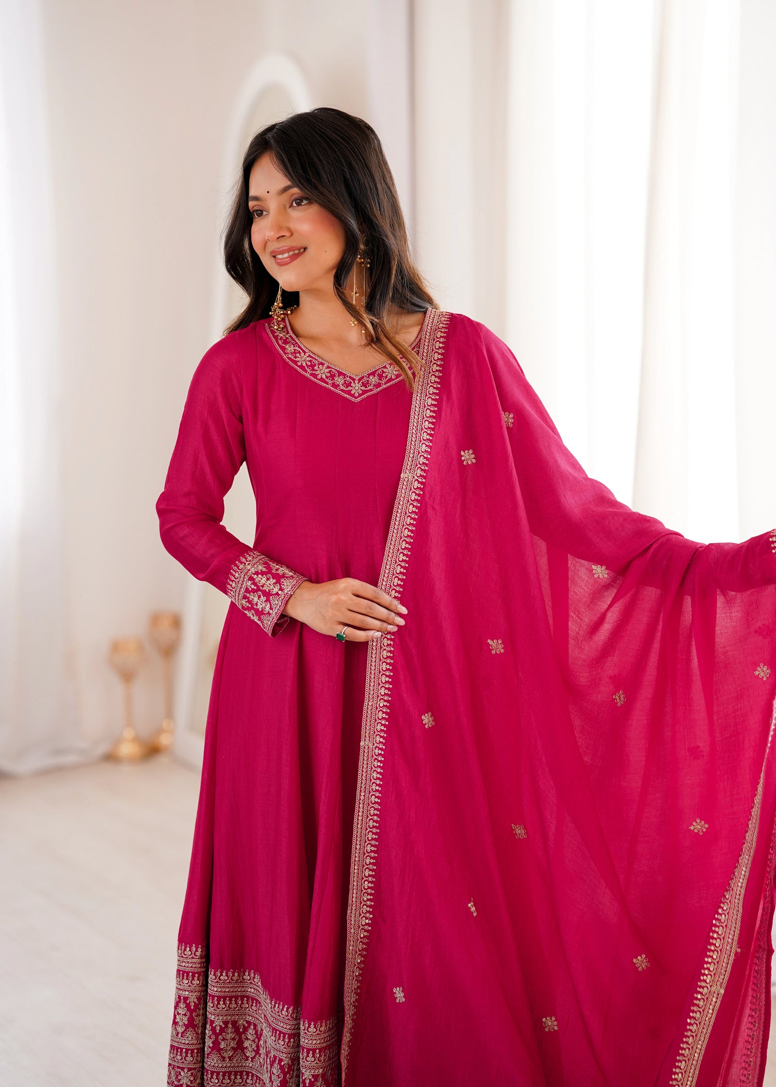 Woman wearing a pink traditional outfit with intricate designs in a softly lit room.