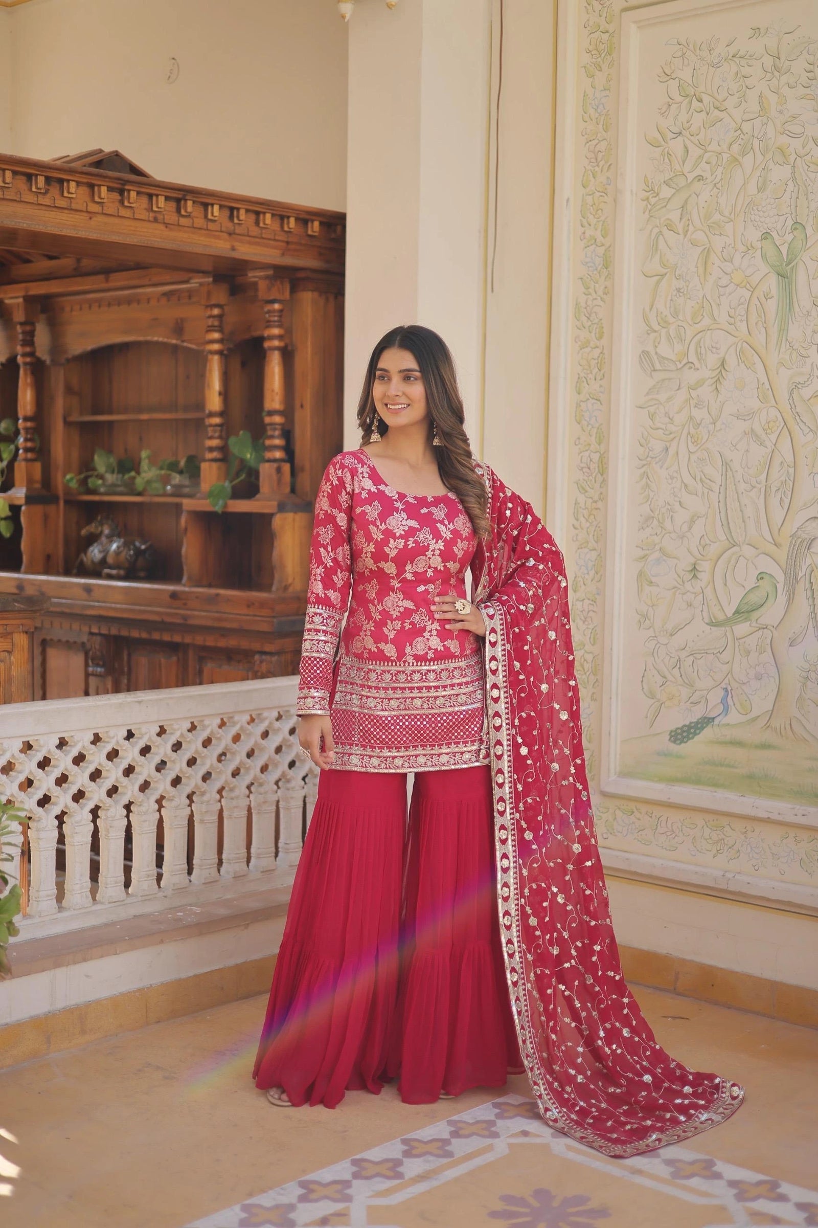 Woman in a red traditional outfit with floral patterns in an ornate room.