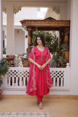 Woman in a pink traditional outfit standing in a decorative indoor setting with wooden architecture and plants.