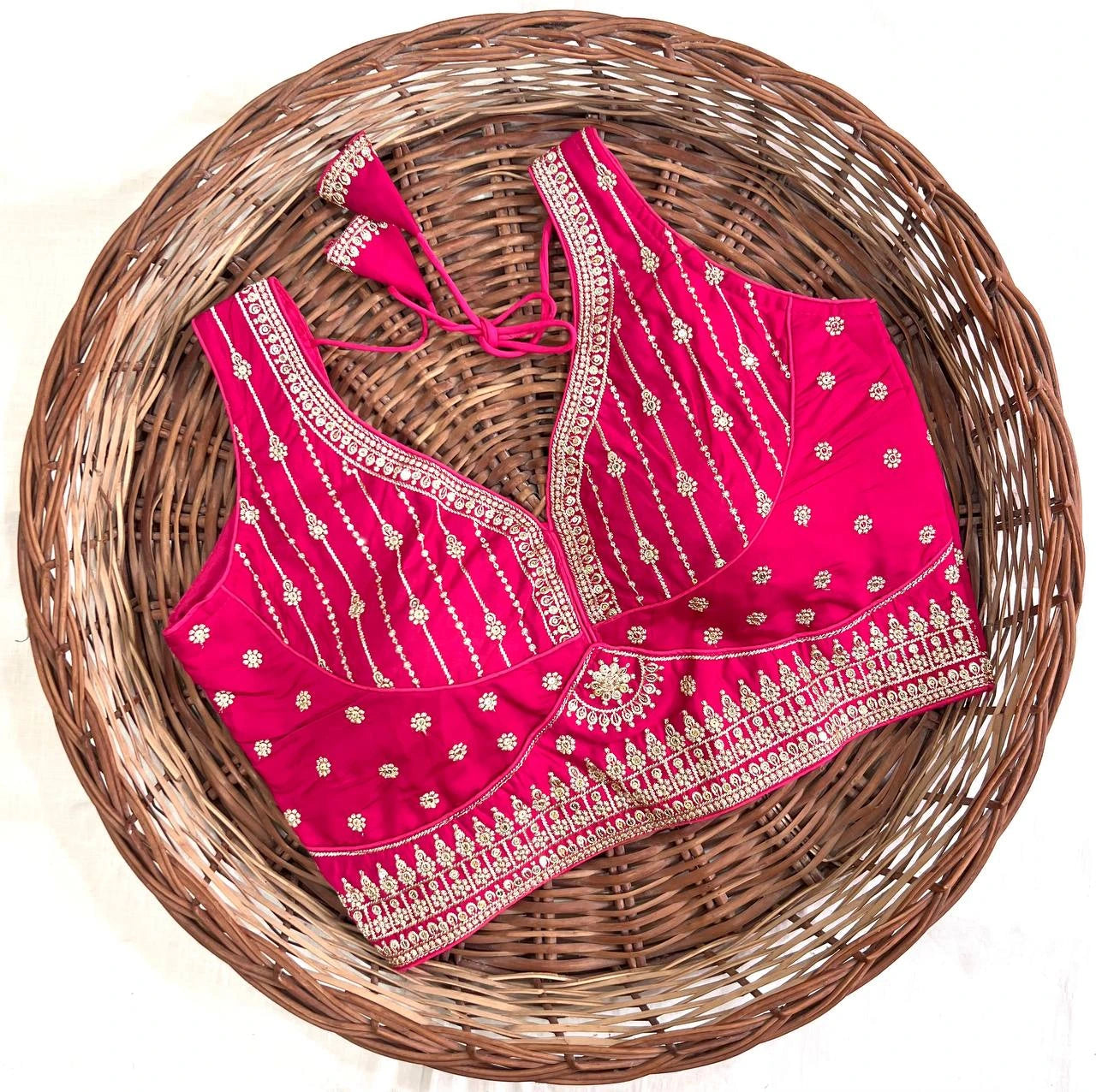 Pink embroidered blouse with gold details on a woven basket